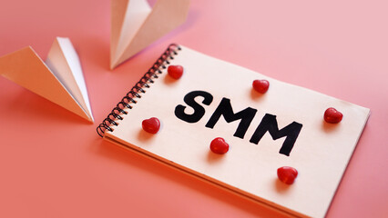 Social media marketing concept. The inscription SMM on a pink background with candy in the form of hearts and paper planes