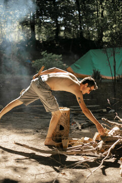 A topless man splitting firewood