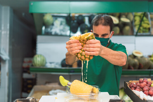 A man squeezing a pineapple in his own fruit shop