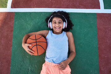A little girl with curly hair is lying on a basketball court laughing