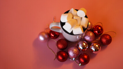 Trendy Christmas background of of hot chocolate with marshmallow, decorated with balls on pink - top view