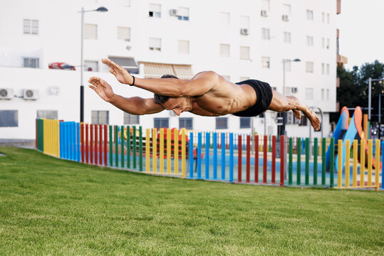 A young man doing calisthenic jumps in a colored park