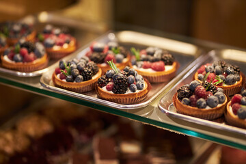 Cakes on a glass counter in a bakery. cakes with fresh berries. tartlets with yogurt, raspberries and blackberries, strawberries and blueberries. Tartlets with raspberries, blackberries.