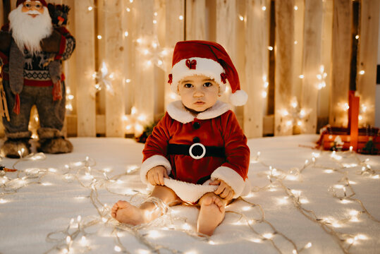 A baby girl sits looking at the camera dressed as a Santa Claus. - Powered by Adobe