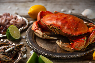 Close-up top view of cooked crab on baby octopuses and tiger shrimps background. Served with lime, lemon and seashells on rustic wooden table. Seafood concept. Delicious meal.