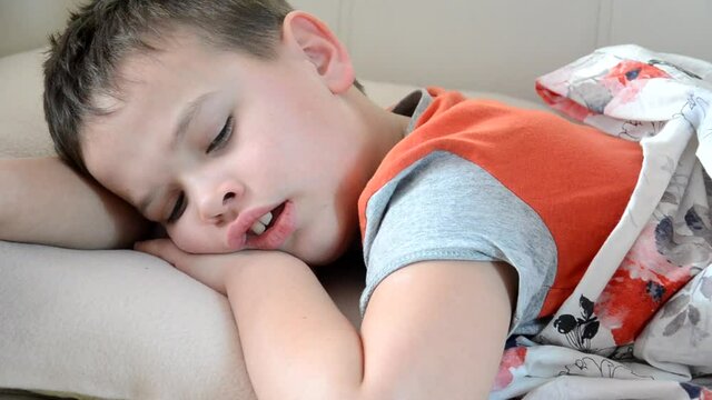 the boy lies at home with a fever, with a cough, is being treated. Sick child boy lying in bed, resting at home mom pours potion into a spoon