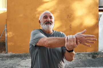 An elderly man with white hair and beard is stretching outdoors