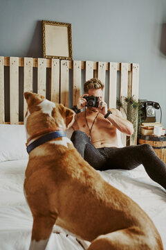 A young blond boy taking pictures of his dog in bed