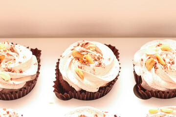 Chocolate muffins with white cream and nuts in an open craft box from above on a white background. Top and side view shot