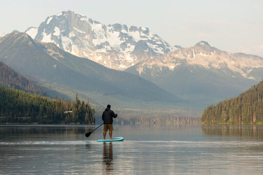 Man on paddle board on calm Duffey Lake in mountains at sunrise.