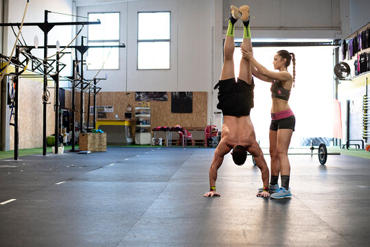 Young trainer helping a muscular man to do a handstand