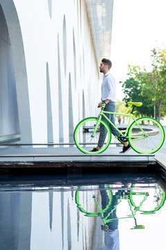 Side view of a young bearded man walking with fixie bike