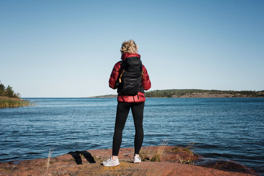 woman staning on a rock with a backpack looking at the ocean & islands