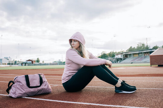 woman sat on a running track with a sports bag waiting