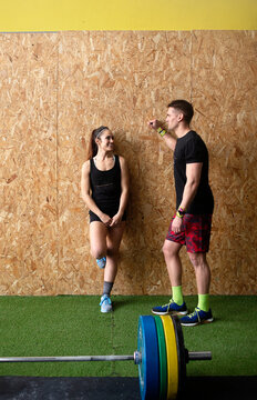 Strong man and woman in sportswear smiling and having nice conversation while leaning on gym wall