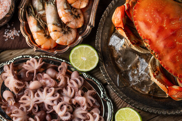 Close-up top view of assorted seafood. Cooked crab with ice-cubes, baby octopuses and tiger shrimps served with lime and seashells on rustic wooden background. Seafood concept. Delicious meal.