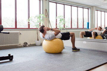man doing sit ups on a fit ball at the gym