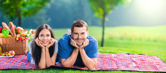 Bright photo of young happy smiling couple, lying together on a picnic blanket, outdoors. Copy space empty place for text. Sunny day picture.