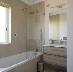 New bathroom with bath, sink and shower screen with beige tiled walls