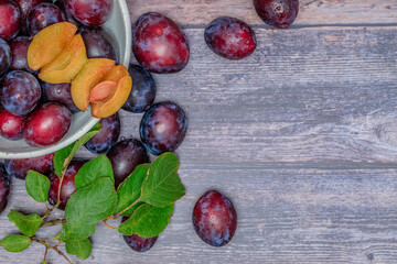 Obraz premium Fresh, ripe plums with green leaves in a metal bowl on a wooden table.