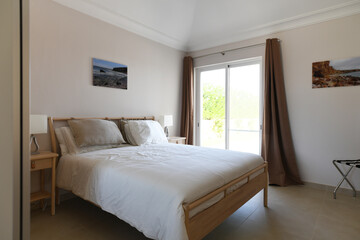 Modern, clean double bedroom with glass sliding doors and white bedding and wooden bed frame