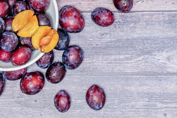 Fresh, ripe plums in a metal bowl on a wooden table.