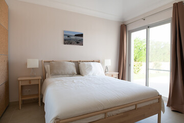 Modern, clean double bedroom with glass sliding doors and white bedding and wooden bed frame
