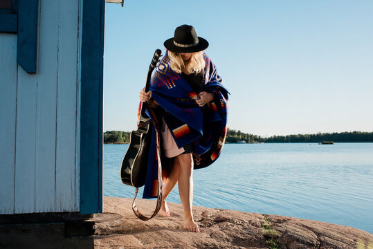 woman wrapped in a blanket holding her guitar at the beach