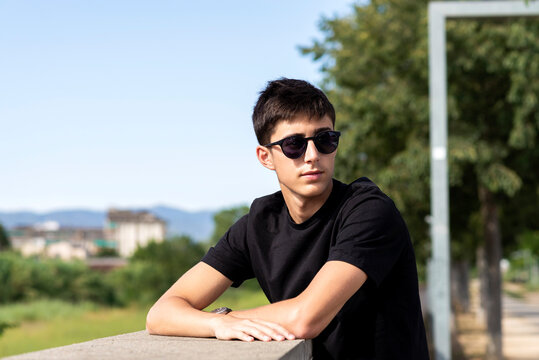 Young guy with sunglasses leaning on wall while looking away