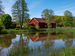 Fototapeta na wymiar Red barn by a lake in Sweden. It is summertime and trees are reflecting in the water