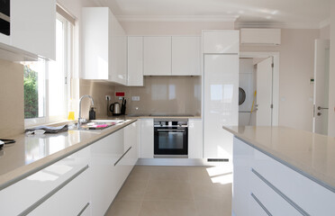 Fototapeta na wymiar Brand new modern kitchen with white cabinets and beige stone counter top and ceramic tiled floor