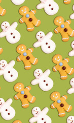 Vertical christmas cookies pattern in the shape of a snowman and a gingerbread man decorated with icing sugar and fondant on a green background