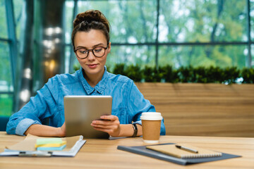 Nice-looking young caucasian businesswoman using tablet at the desk in modern office