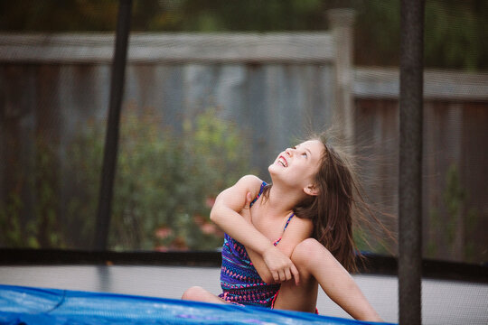 A laughing child with wild hair plays in a trampoline in her yard