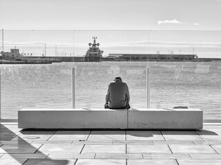 Hombre mayor sentado solo en un banco mirando el mar