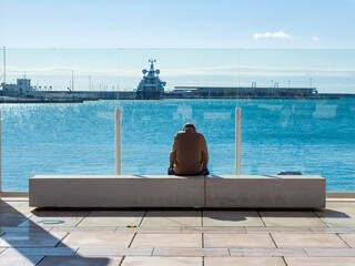 Hombre mayor sentado mirando el mar en el puerto