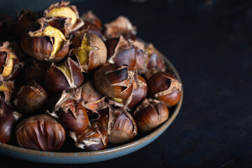 Roasted chestnuts in ceramic dish on dark background. Winter background.