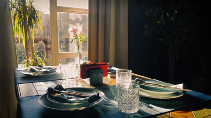 Table setting for romantic breakfast in the morning sun through a window. Shadows and sunbeams in dark room.