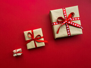 Top view, copy space, red background. Christmas gift boxes wrapped with craft paper and red ribbons.