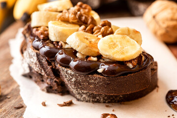 Toast with rye bread, chocolate, bananas, and walnuts on a wooden table. Close-up, selective focus.