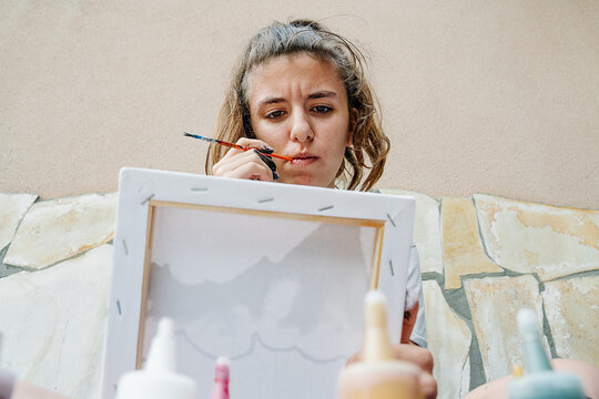 white girl sucking a painting brush while thinking of how continue her picture. Horizontal photo
