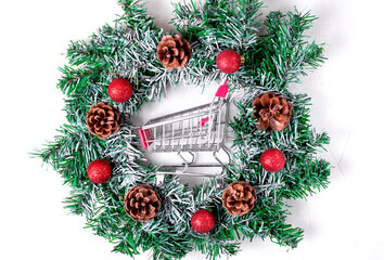 Shopping cart in Christmas wreath with cones and red baubles. Top view. Concept of Christmas and New Year shopping