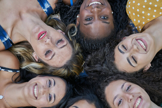 A group of six smiling friends lying down and looking up at the camera