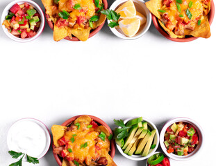 Nachos with chicken, mushroom and melted cheese in portion bowls served with assorted toppings on white table. Top view. Mexican food. Copy space