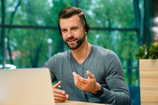 Friendly helpful young man with headset explaining information on laptop at office desk
