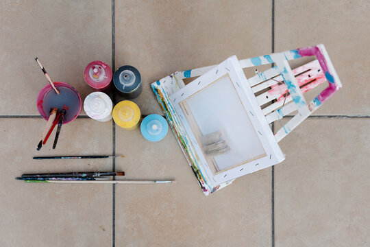 painting bottles, brushes, easel and picture on the floor of a terrace. Overhead horizontal photo
