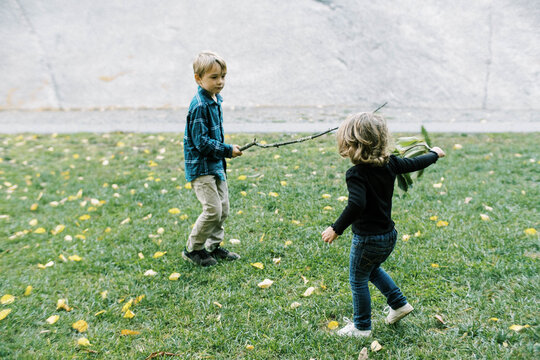 Two kids playing with sticks in a park together