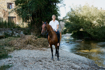 Portrait of a young blond man riding a horse over a river