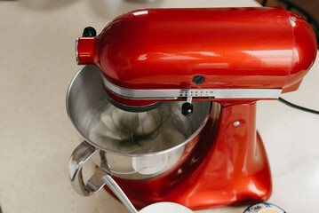 A close photo of a red stand mixer which is whipping the egg whites in a stainless steel soup bowl in a kitchen.