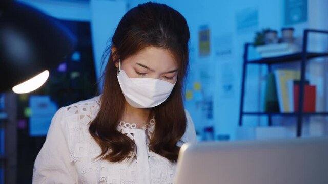 Freelance Asia women wear face mask using laptop hard work at new normal home office. Working from house overload at night, self isolation, social distancing, quarantine for corona virus prevention.